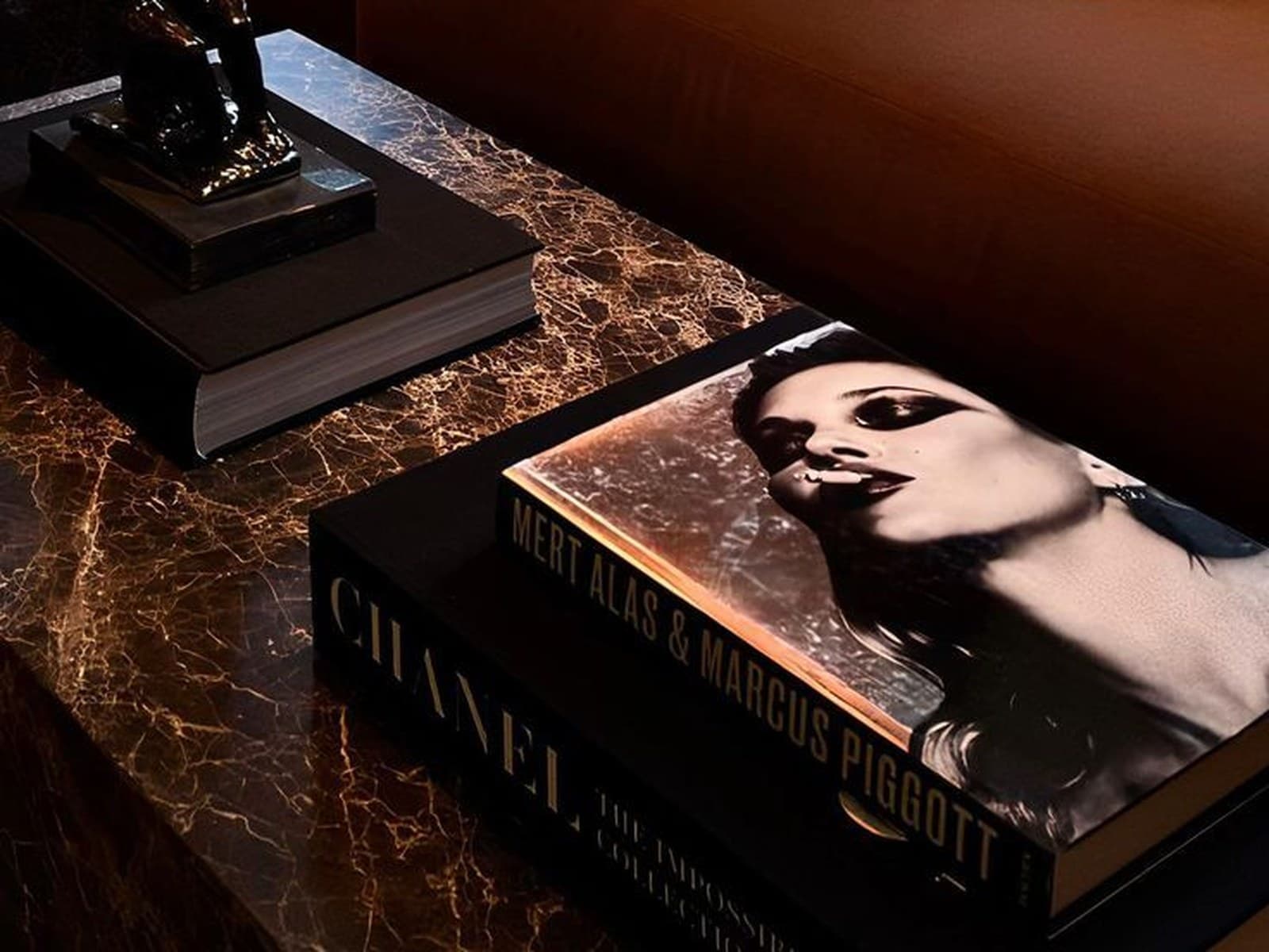 Маленькая бронзовая статуэтка и стопка дизайнерских книг для журнального столика на тёмном мраморном столе