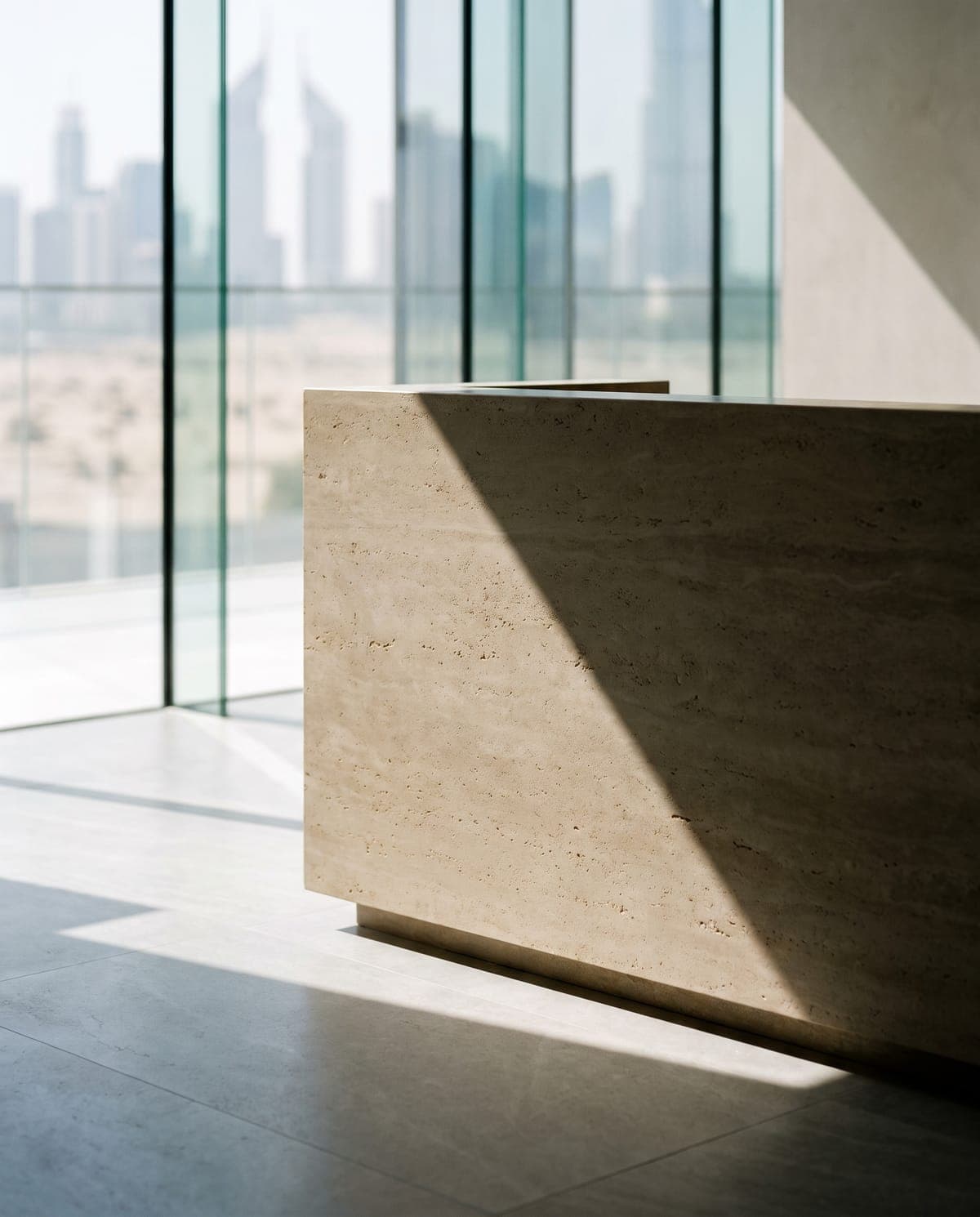 A stone reception desk inside a Dubai brokerage, the city skyline visible through floor-to-ceiling glass.