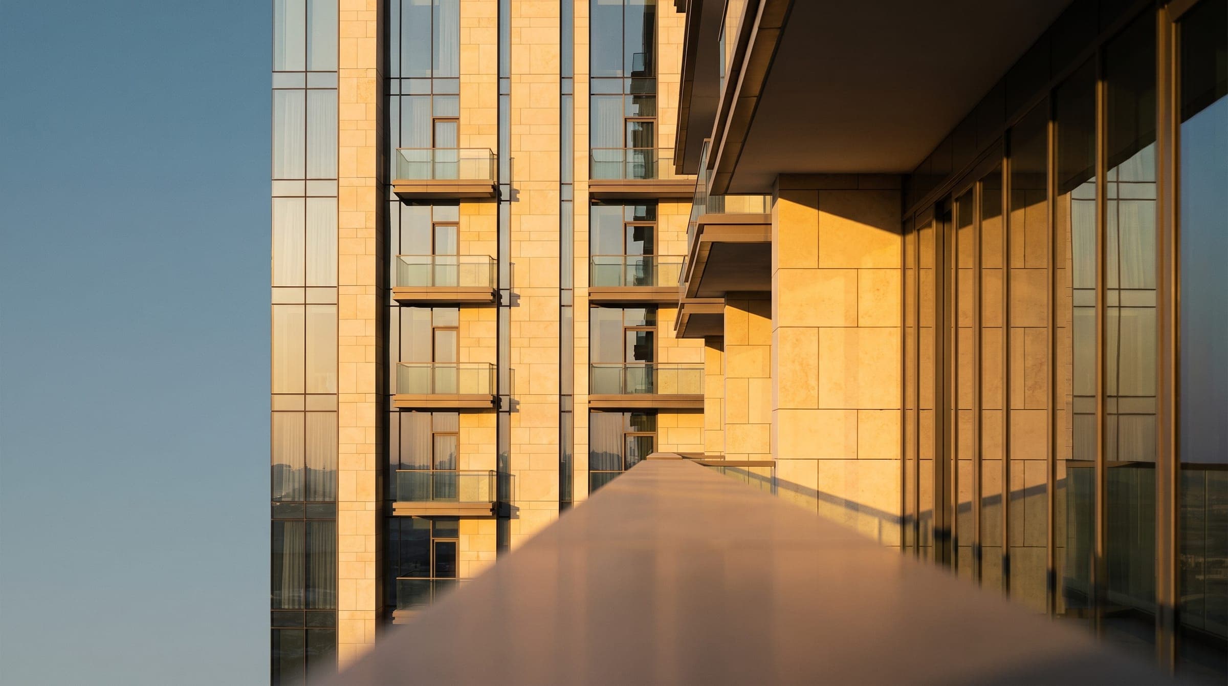A residential tower's honey-limestone facade and private terraces catching golden-hour light, Dubai.
